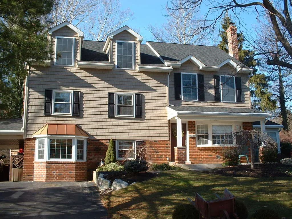 Two-story house with three dormers, cedar-shake siding over a brick base, and a bay window